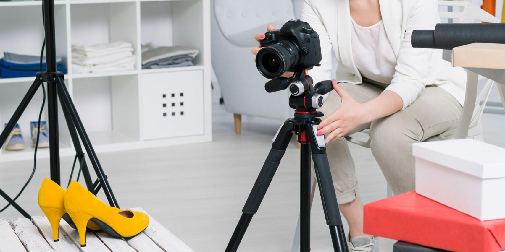 Young fasioner making photo of high-heeled shoes using the lamp and a tripod in her atelier
